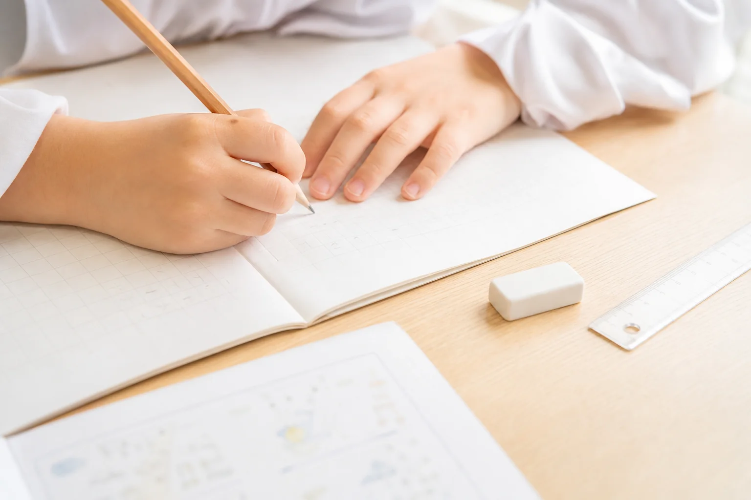 机の上で方眼ノートに鉛筆で筆算を書いている子どもの手元